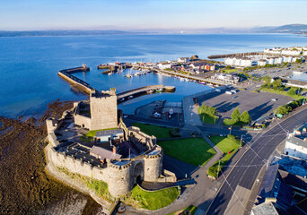 Medieval Norman Castle in Carrickfergus near Belfast in sunrise light. Aerial view with marina, yachts, parking, town and far view of Belfast in the background. - 457844565