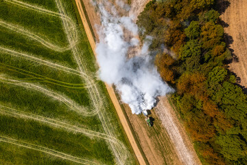 Aerial view of a tractor spreading lime on agricultural fields to improve soil quality after the...