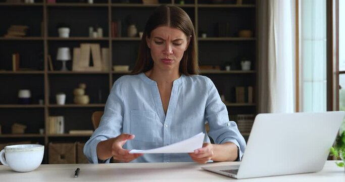 Nervous annoyed female self employed entrepreneur read papers at home office workplace distressed with bad news debt bankruptcy. Frustrated young lady hold bank notice with loan rejection tax overdue