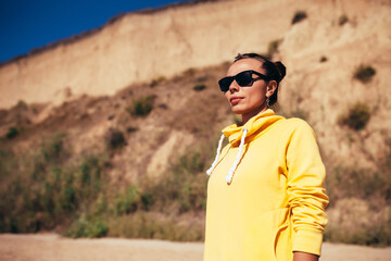 Handsome young female wearing yellow blank hoodie or sweatshirt and sunglasses at the tropical beach. Mock-up for print.