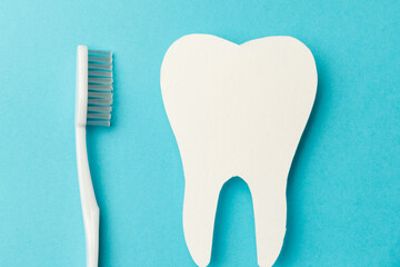 The concept of the International Day of the Dentist. A white toothbrush and a paper tooth on a blue background. Top view. Flat lay. Close-up. Copy space