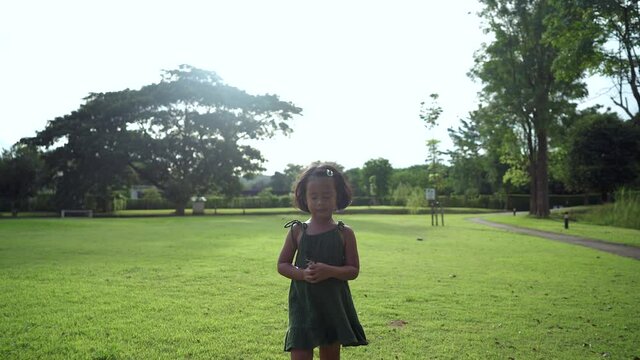 Active small girl in green dress  walking at field against sun light background.