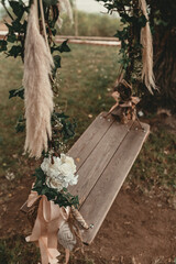 A wooden swing decorated with flowers hangs on a tree in the yard. Wedding decoration