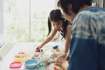 Asian girl in casual dress having fun while make pizza with prosciutto, tomato, cheese, vegetables in home kitchen. family and relationship concept