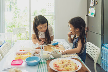 Asian girl in casual dress having fun while make pizza with prosciutto, tomato, cheese, vegetables in home kitchen. family and relationship concept