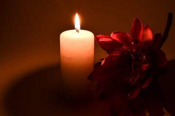 Czerwony, sztuczny kwiat i paląca się świeczka. - obrazy, fototapety, plakaty