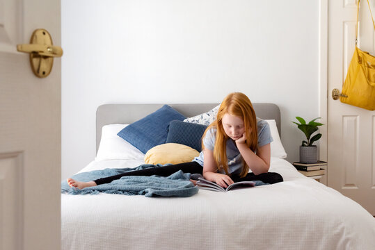 Red haired girl on white bed reading