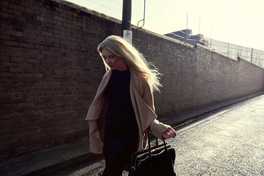 Girl walking down street alley backlit by sun next to brick wall