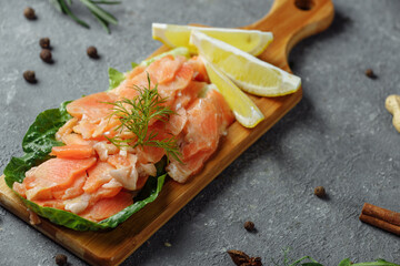 Pieces of fried salmon with dill and lemon wedges on a wooden board