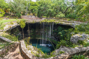 Fototapeta na wymiar Hermosa vista de una cascada sobre plantas verdes en un cenote, en Yucatán, México