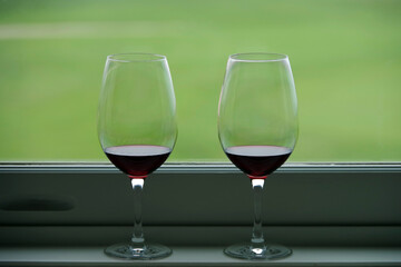 Two glasses with red wine on a green window sill and green lawn behind