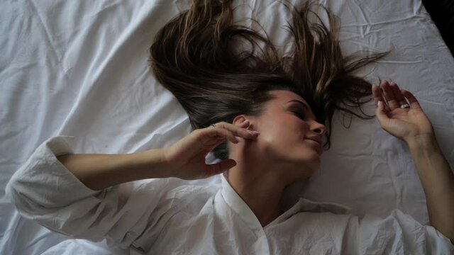 beautiful woman brunette sensually strokes her hands lying on white bed linen. High quality FullHD footage