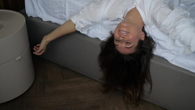 a young brunette woman lies on the bed in a white shirt upside down and makes movements with her hands. High quality FullHD footage