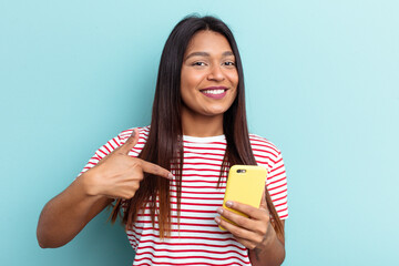 Young Venezuelan woman holding mobile phone isolated on blue background person pointing by hand to a shirt copy space, proud and confident