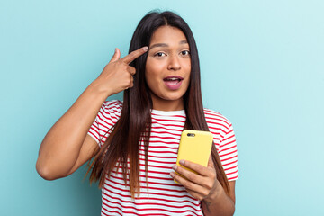 Young Venezuelan woman holding mobile phone isolated on blue background showing a disappointment gesture with forefinger.