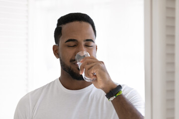 Young African man in white t-shirt drinks still water, head shot. Water balance and weight control,...