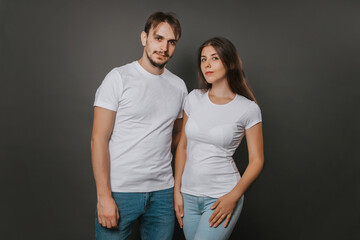 A young couple, a girl and a man in white blank t-shirts on a dark gray background. Mock-up. love story