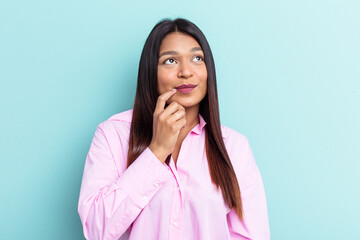 Young Venezuelan woman isolated on blue background looking sideways with doubtful and skeptical expression.