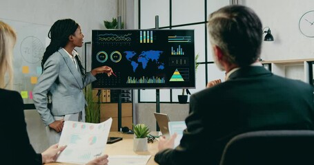 Close up of likable positive confident qualified black-skinned woman which explaining presentation of world economic growth of production on digital screen for attantive successful male and female