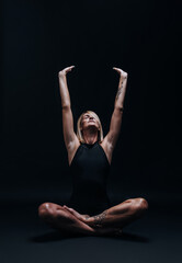 Obraz premium a forty-year-old woman in excellent physical shape with elastic muscles and healthy skin performs yoga exercises on a dark background. Studio photography. excellent health at forty.
