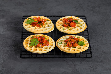 Unsweetened snack waffles with baked cherry tomatoes and parsley on a serving metal stand on a dark gray background 