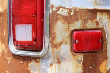 Old rusty car with broken red lights with visible metal corrosion. Trash that could possibly be recycled.