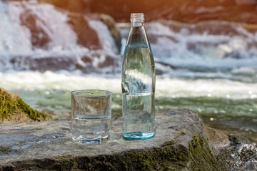 Natural drinking water in a bottle and glass beaker on nature background river