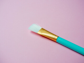 A blue cosmetic brush for applying face masks lies on a pink background. Close up