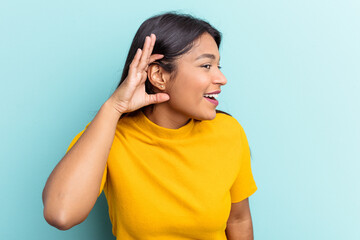 Young Venezuelan woman isolated on blue background trying to listening a gossip.