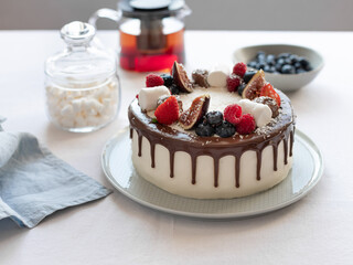 closeup of fresh delicious cake with berries, marshmallows and teapot on linen tablecloth. Birthday, Mothers Day concept.