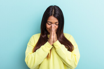 Young Venezuelan woman isolated on blue background praying, showing devotion, religious person looking for divine inspiration.