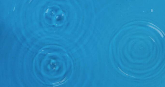 Three drops of rain fall into blue water. Top view. Drop falls into water and diverging circles of water