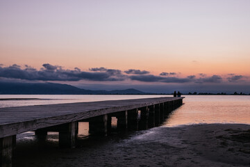 Fototapeta na wymiar Anonymous persons sitting on pier near sea at sunset
