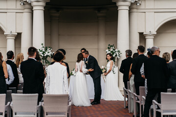 Candid shot of father walking his lesbian LGBT daughter through aisle towards her bride. Shot with 2x anamorphic lens