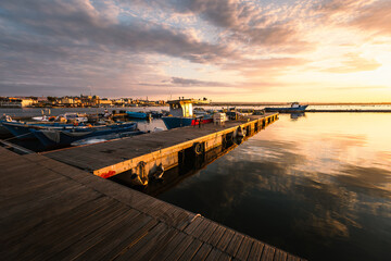 Taranto Vecchia pier at dawn with orange sky with clouds and moored boats