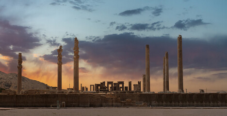 Ruins of Apadana and Tachara Palace behind stairway with bas relief carvings in Persepolis UNESCO World Heritage Site against cloudy sunset sky in Shiraz city of Iran.