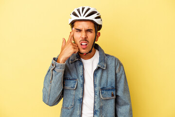 Young mixed race man wearing a helmet bike isolated on yellow background showing a disappointment gesture with forefinger.