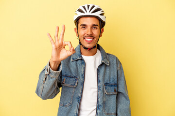 Young mixed race man wearing a helmet bike isolated on yellow background cheerful and confident showing ok gesture.