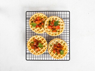 Unsweetened snack small waffles with baked cherry tomatoes and parsley on a serving metal stand on a light background top view