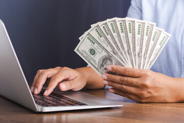 A young man with dollar banknotes in his hand and working using a laptop. Business and investment concept