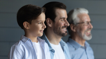 Head shot profile of three generations of men standing in row on grey studio wall background,...