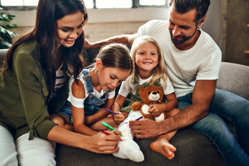 Little girl with a broken leg on the couch. Mom, dad and two daughters draw on plaster with...