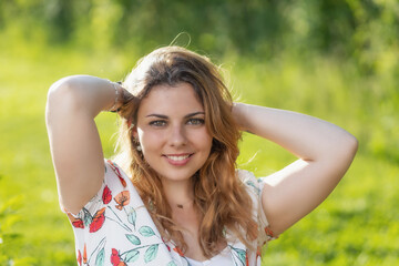 Smiling beautiful  young woman with both hands in her hair is posing outdoors. Horizontally. 