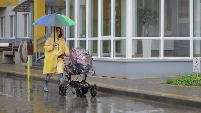 Mom with a stroller in a yellow raincoat walks in the rain
