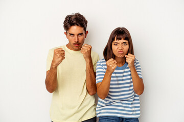 Young mixed race couple isolated on white background showing fist to camera, aggressive facial expression.