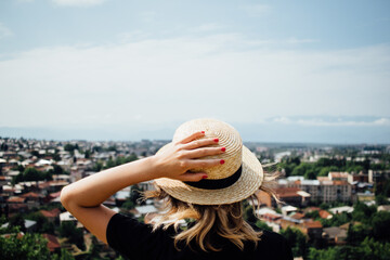 A girl in a straw hat with red nails stands and looks at the cityscape of the city of Kutaisi in Georgia