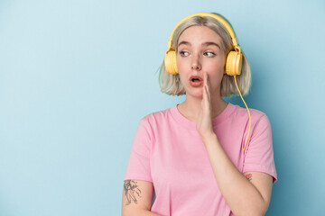 young caucasian woman listening to music isolated on blue background is saying a secret hot braking news and looking aside