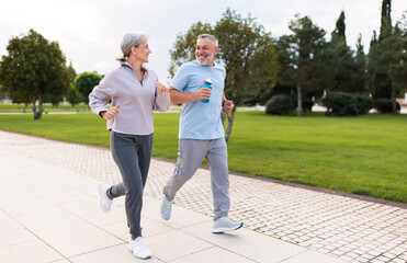 Full-length photo of lovely joyful retirees couple jogging outside in city park