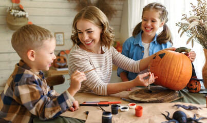 Fototapeta premium Smiling mother with children creating jack-o-lantern during Halloween celebration at home