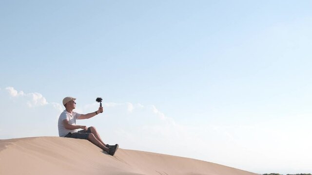 Man filming himself with his cell phone in the desert dunes. Traveling male content creator
